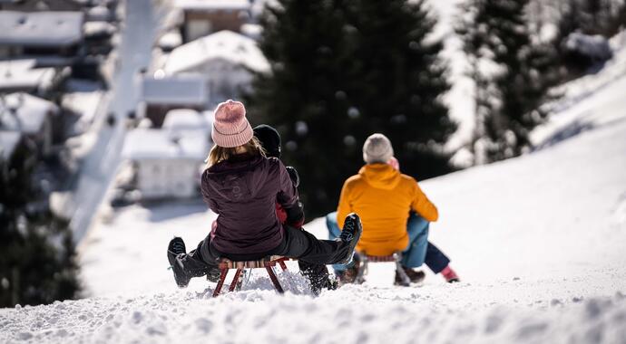 Kinder rodeln auf Schlitten einen schneebedeckten Hügel hinunter