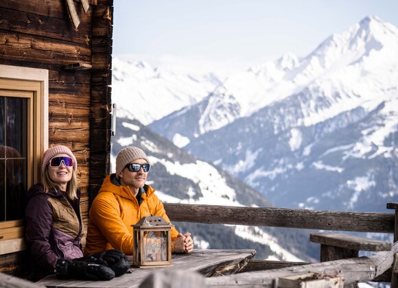 Paar sitzt auf Berghütte mit Blick auf schneebedeckte Berge