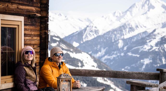 Paar sitzt auf Berghütte mit Blick auf schneebedeckte Berge