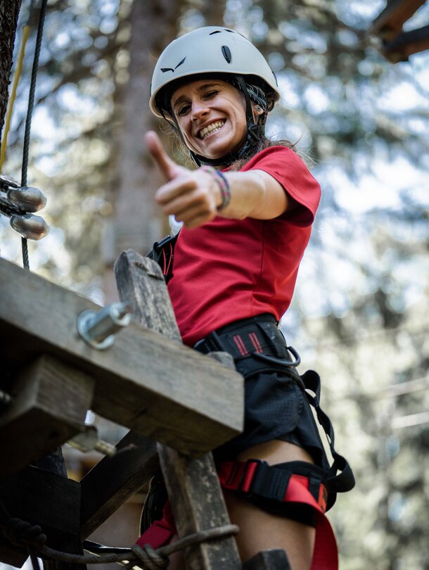 Frau mit Helm und Klettergurt zeigt Daumen hoch im Kletterpark