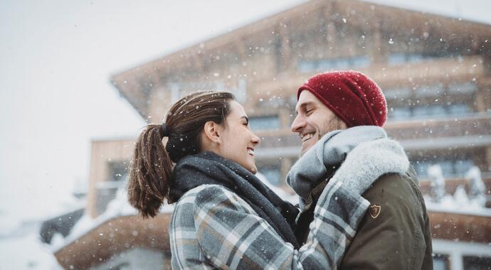 Smiling couple hugging in the snow in front of a house