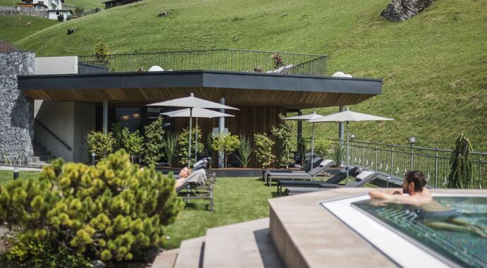 Außenbereich mit Liegen, Sonnenschirmen und Pool vor grüner Berglandschaft