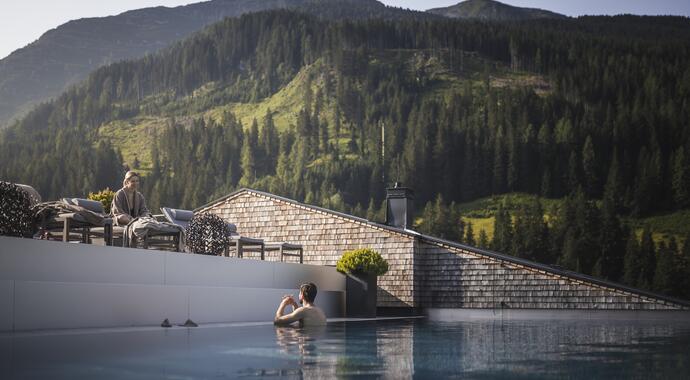 Mann im Pool vor Hotel und bewaldetem Berg
