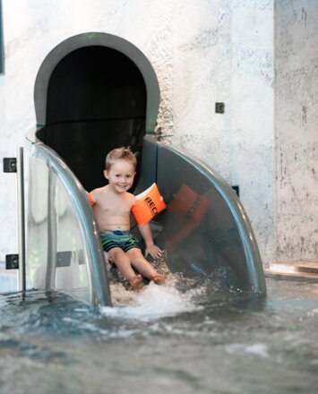 Kind rutscht mit Schwimmflügeln fröhlich auf der Wasserrutsche im Tuxerhof