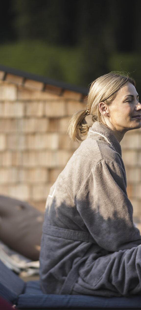 Woman relaxing in a bathrobe outside the Tuxerhof in morning sunshine