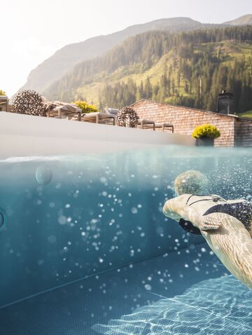 Frau schwimmt in Pool vor Bergpanorama
