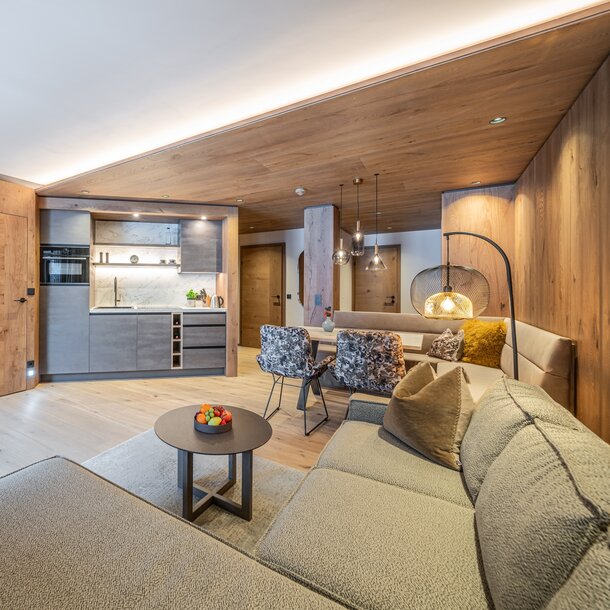 Modernes Wohnzimmer mit Küchenzeile, Sofa, Tisch und Stühlen in warmen Holztönen